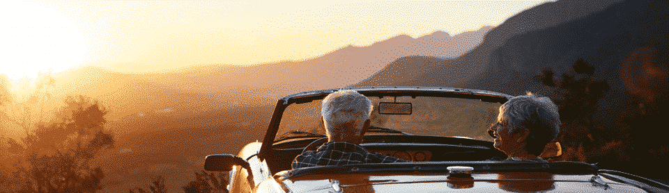 Retired couple looking at sunset in classic car